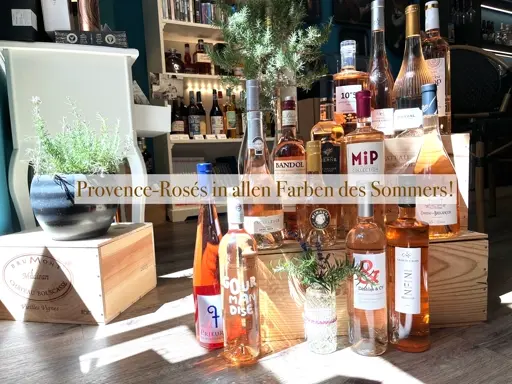 Verschiedene Roséweine in Holzboxen und Flaschen mit grünen Kräutern als Deko arrangiert