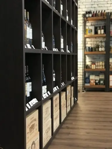 Schwarze Regale mit Weinflaschen in Holzfächern und Etiketten auf den Regalbrettern.