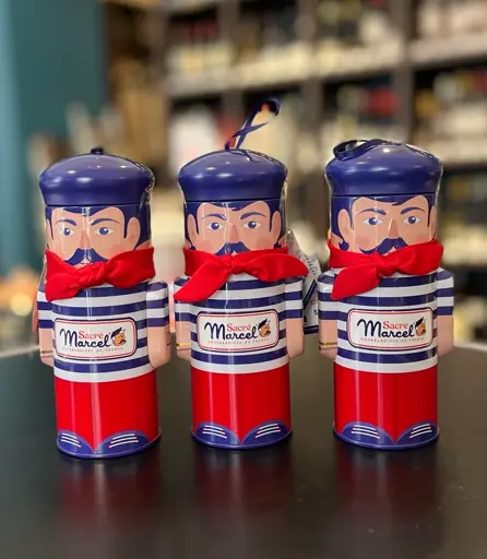 Drei bunte, figurierte Dosen mit Gesichtern, roten Bändern und blauen Hüten, auf schwarzem Untergrund.